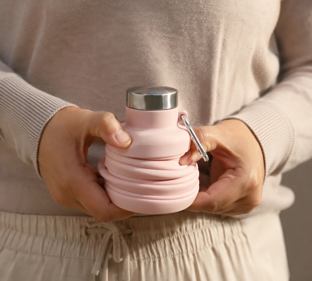 Two hands twisting a Blush Squishly collapsible bottle closed along its accordion rings