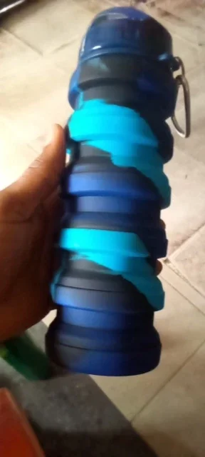 Blue and teal marbled collapsible water bottle pressed down compact, held in a buyer's hand over a tiled floor — photo from a verified buyer