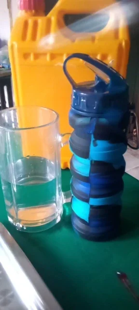 Blue collapsible water bottle with a flip-spout lid standing on a table next to a clear glass of water — photo from a verified buyer