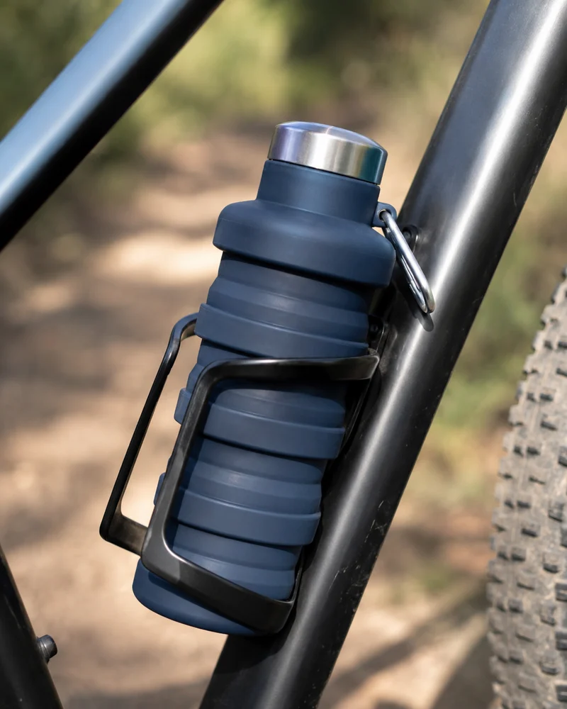 A Slate collapsible water bottle strapped into a bike frame cage on a trail