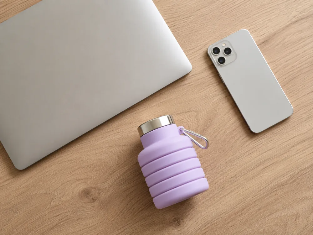 A folded Lavender collapsible bottle on a desk beside a laptop and a phone, taking almost no room
