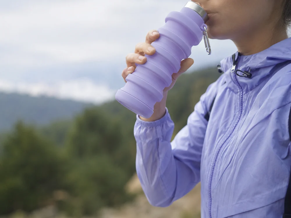 A woman drinking from a Lavender collapsible bottle on a mountain trail